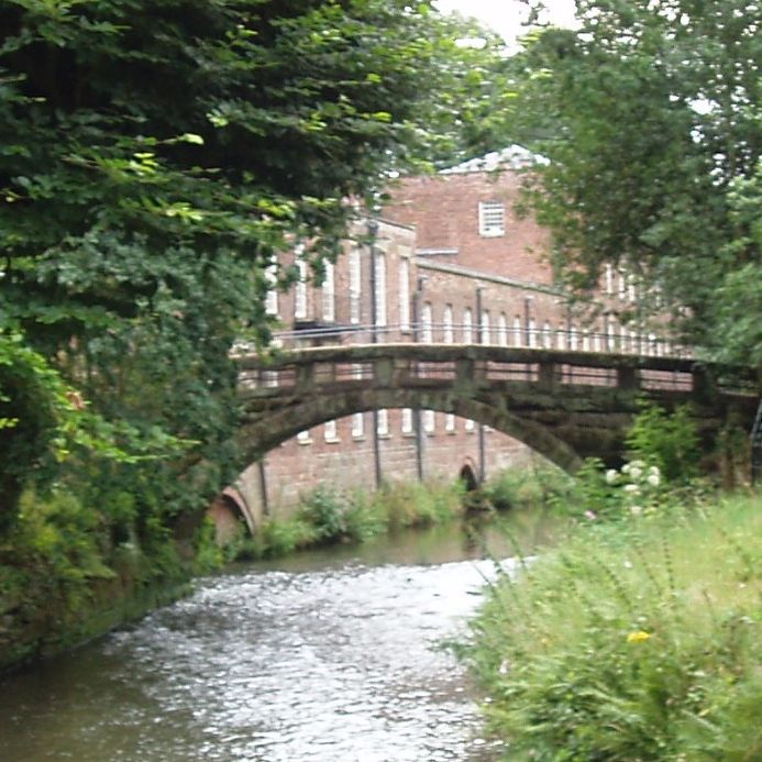 Eine alte Steinbrücke, eingebettet in malerische Natur. Im Hintergrund ein altes Fabrikgebäude